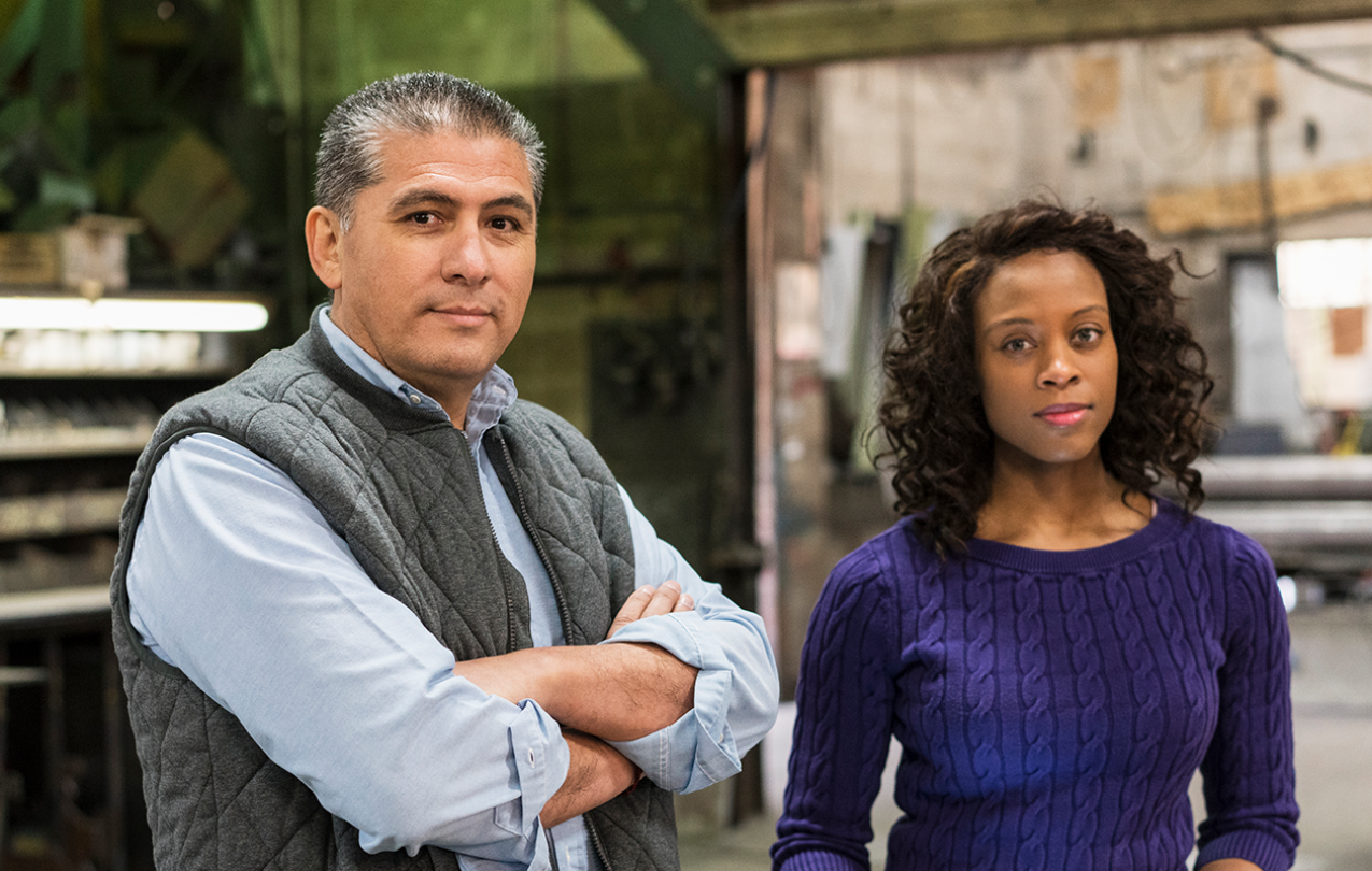 Photo of a man with his arms crossed standing next to a woman with curly hair.